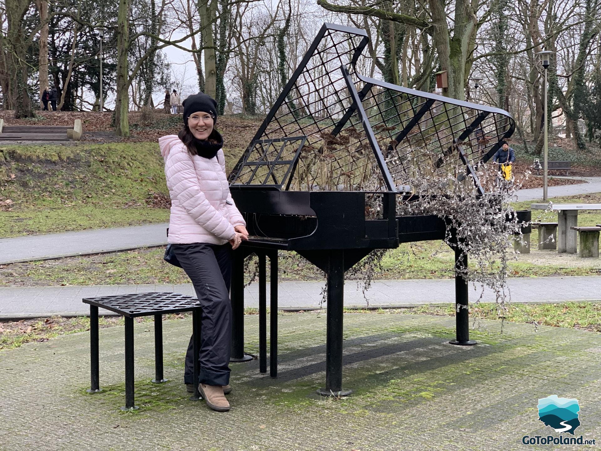sculpture of a metal piano in the park, a woman is standing by it