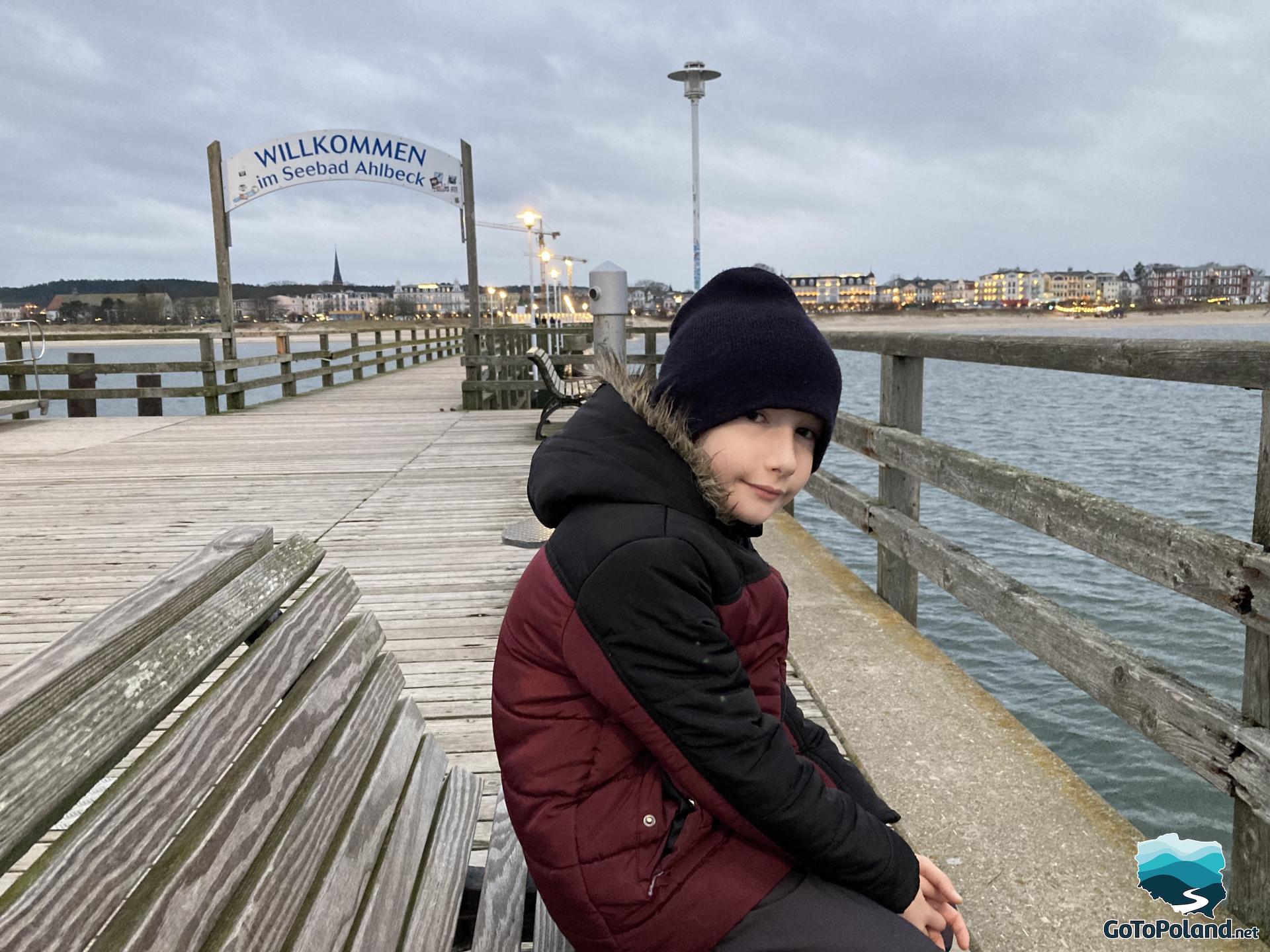 a boy is sitting on a bench on a pier