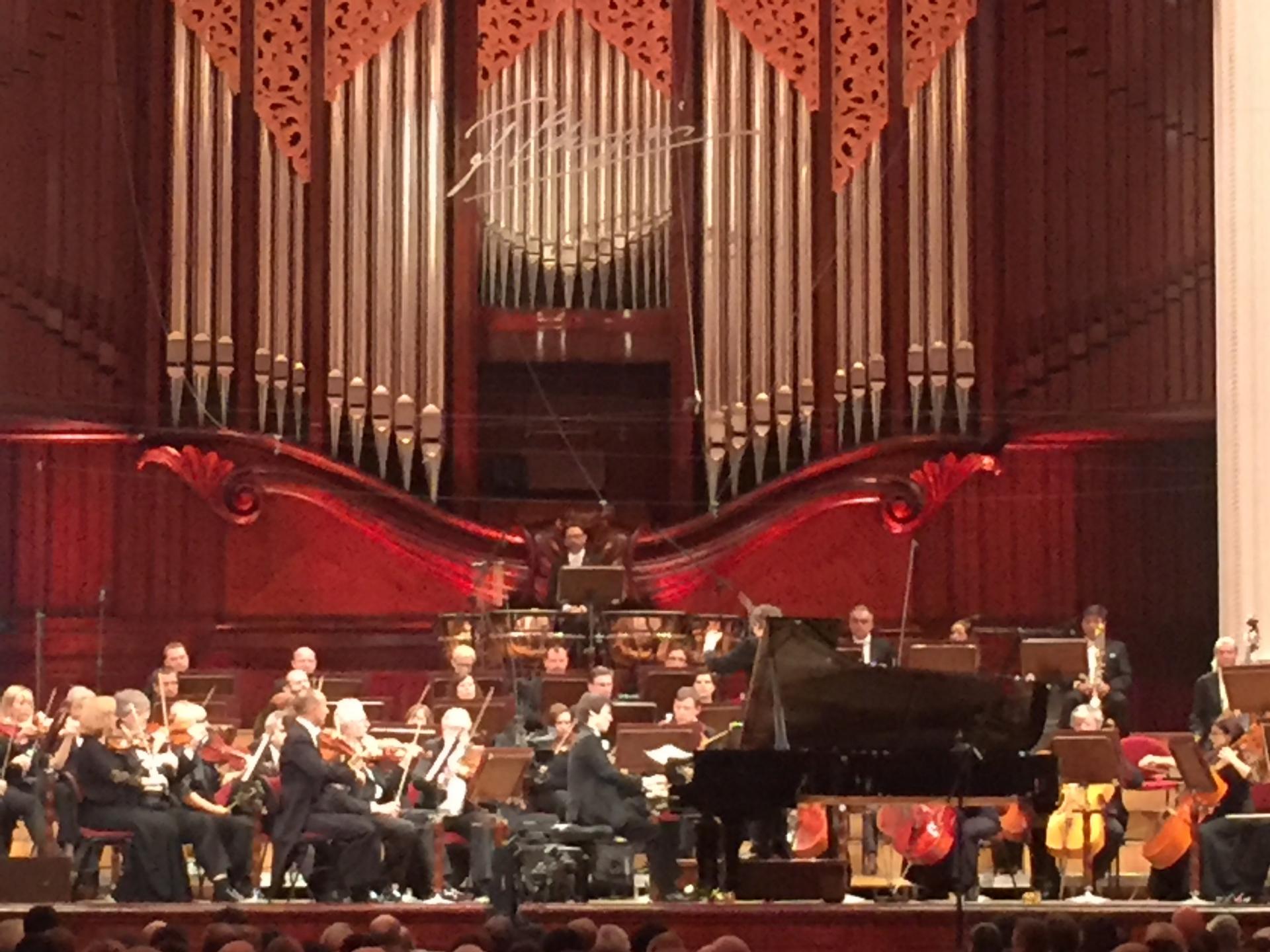philharmonic hall with an orchestra on stage and a pianist playing the piano
