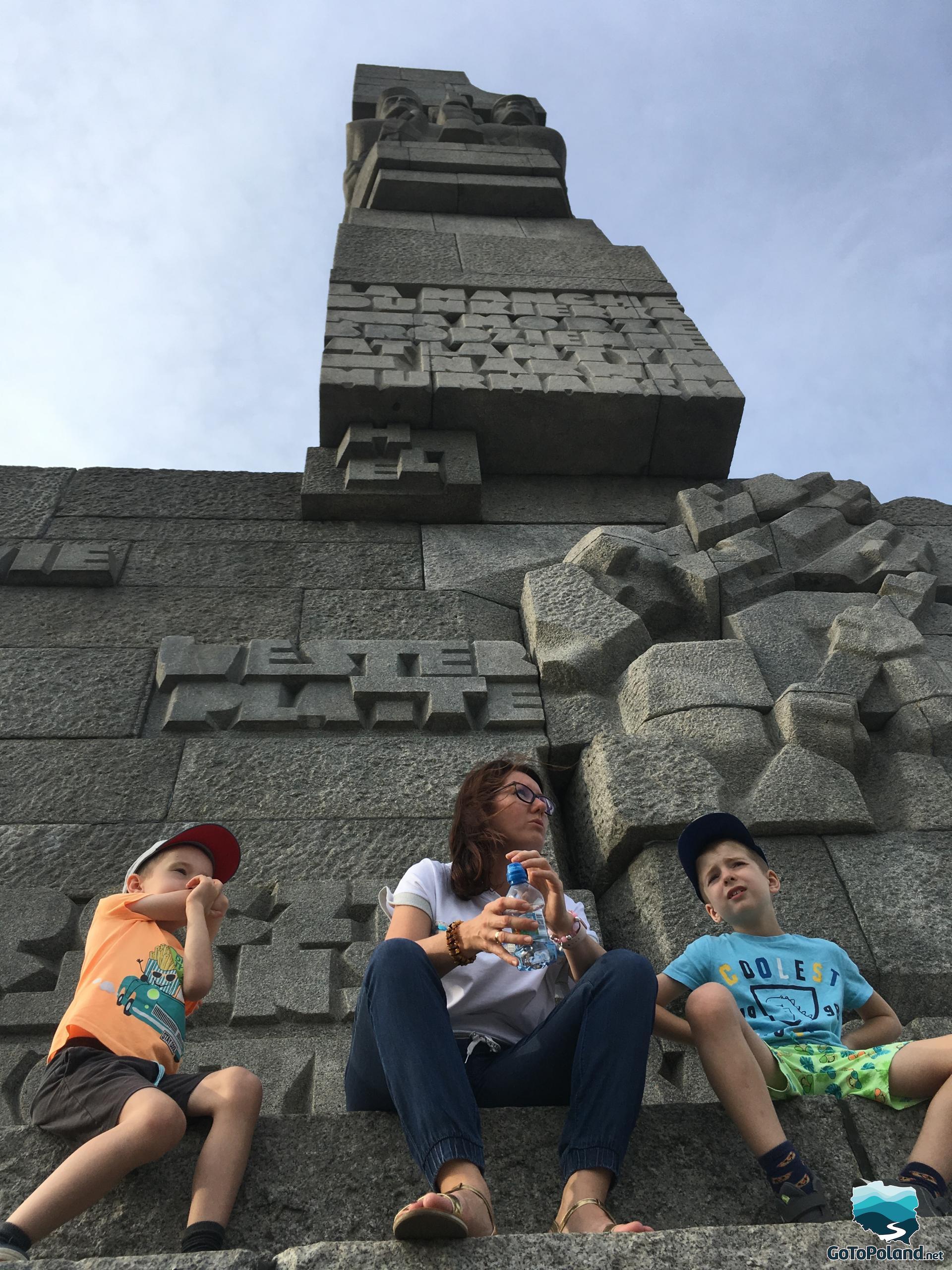 a woman and two children are sitting at the feet of a large monument