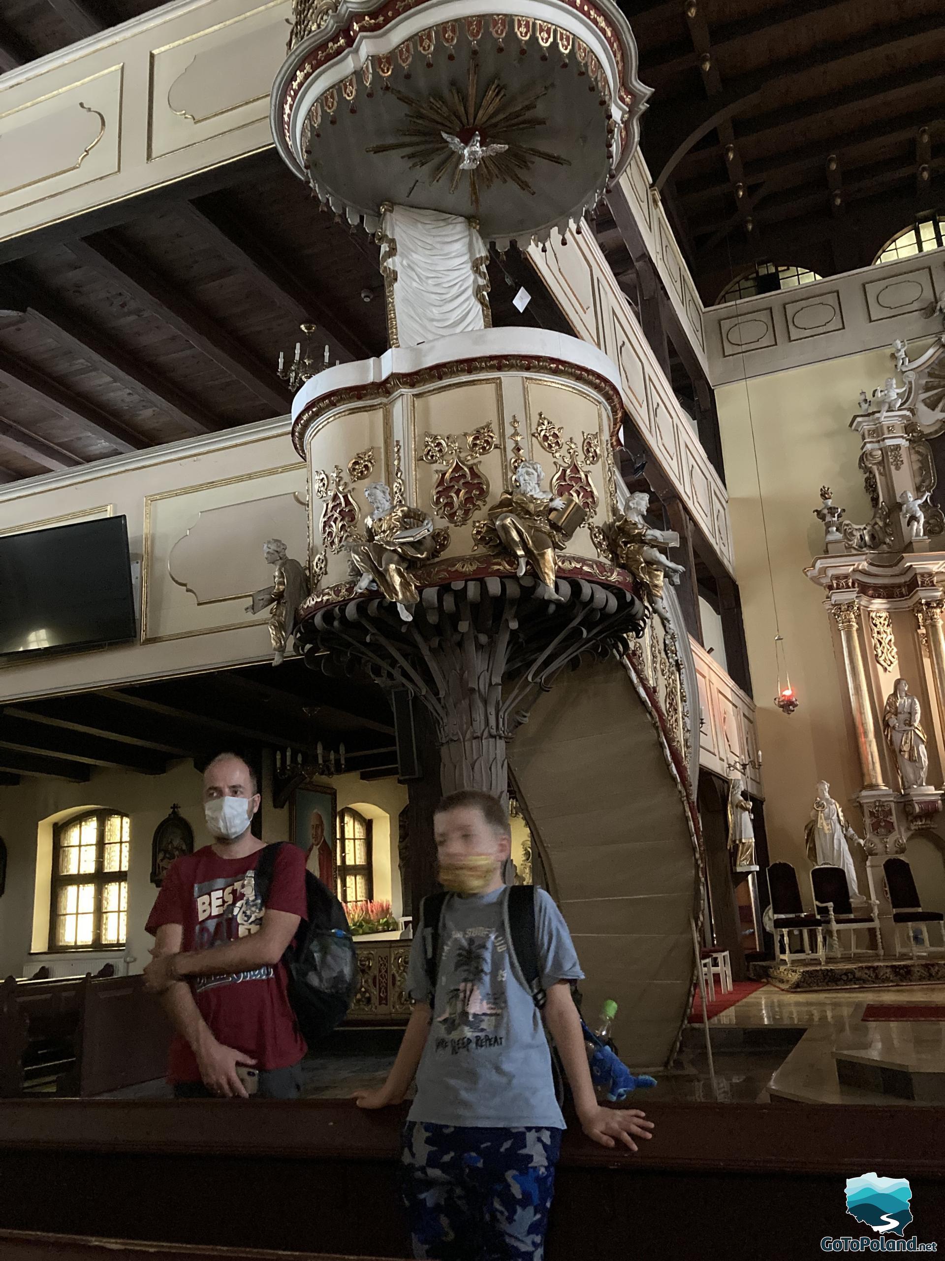 A man and a boy standing inside the church next to a wooden pulpit