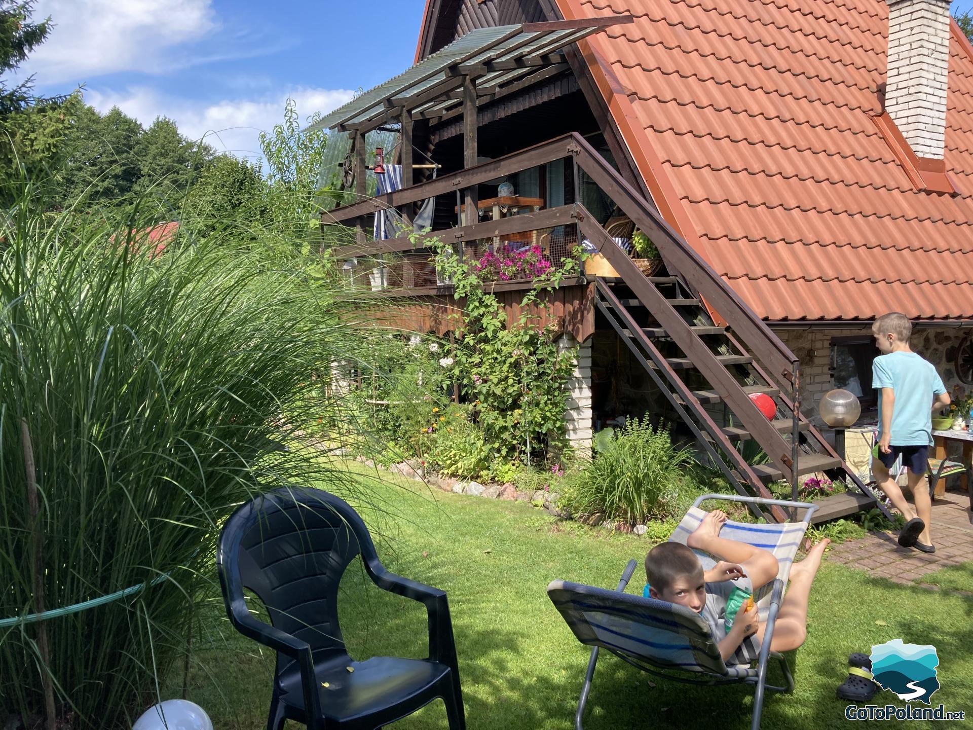 A summer house in the background, one boy is lying on a sunbed