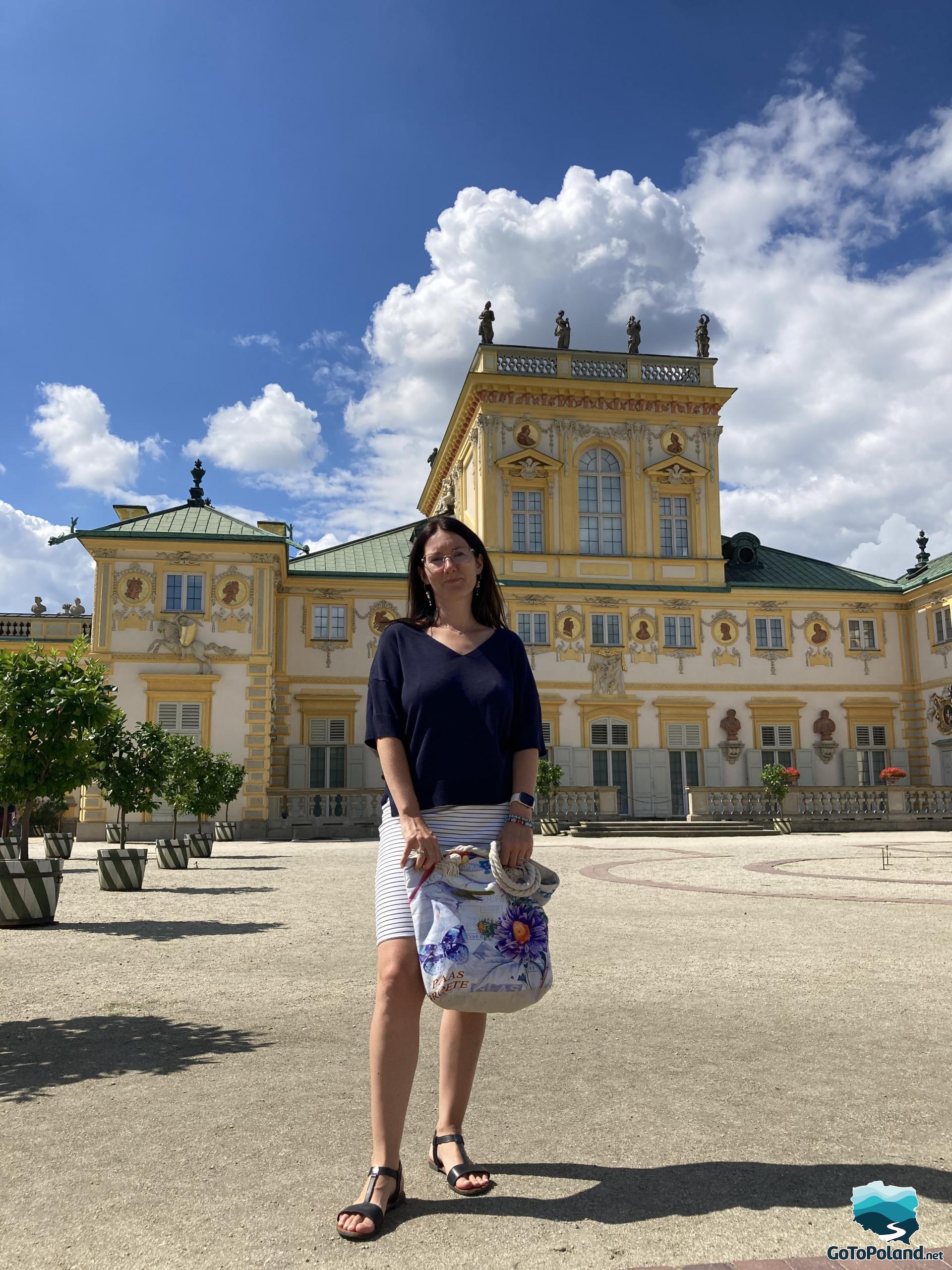 A woman in front of a yellow bulding in which is a palace