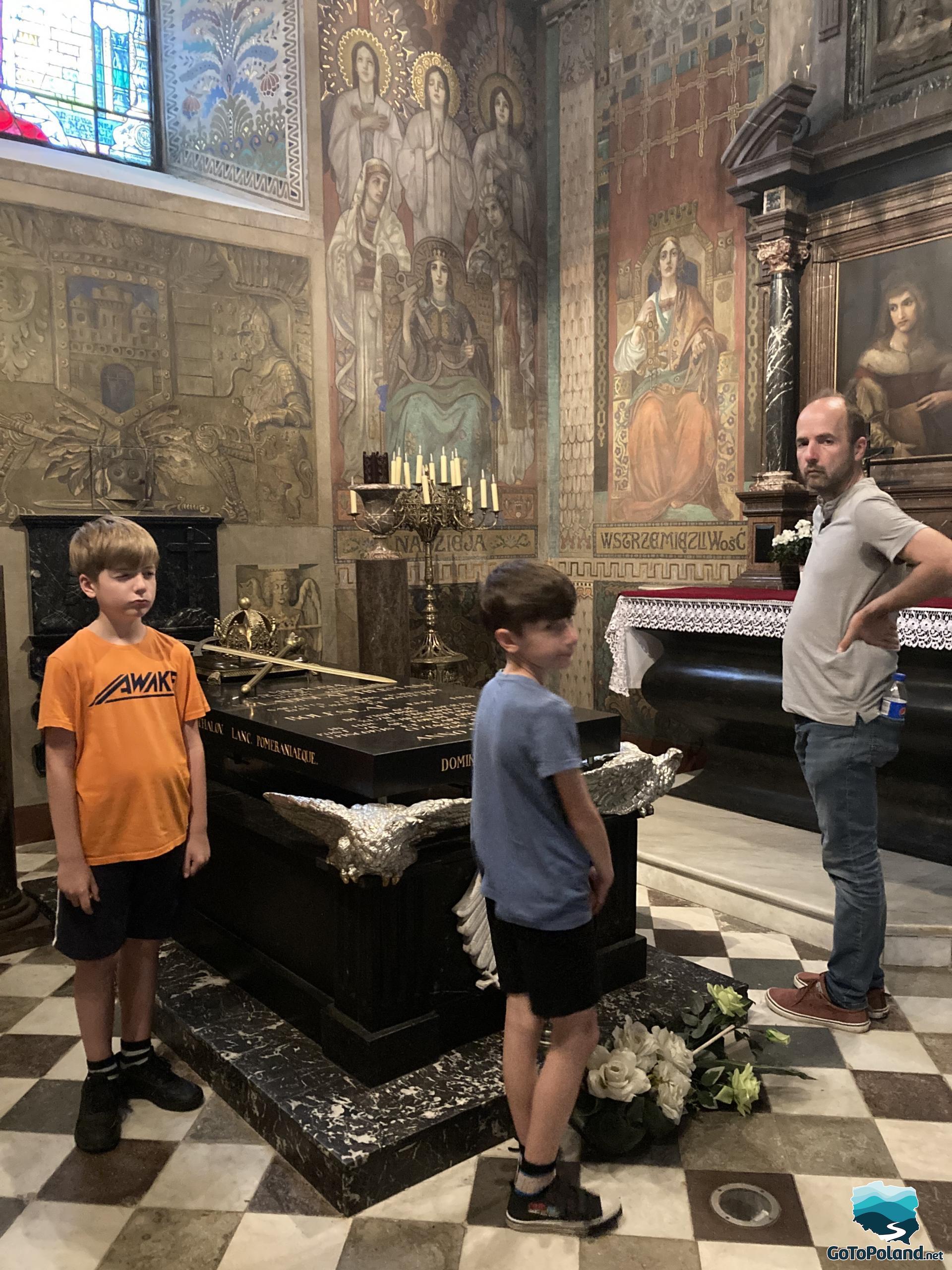 A man and two young boys standing by the tomb of the rulers of medieval Poland. They are in a church