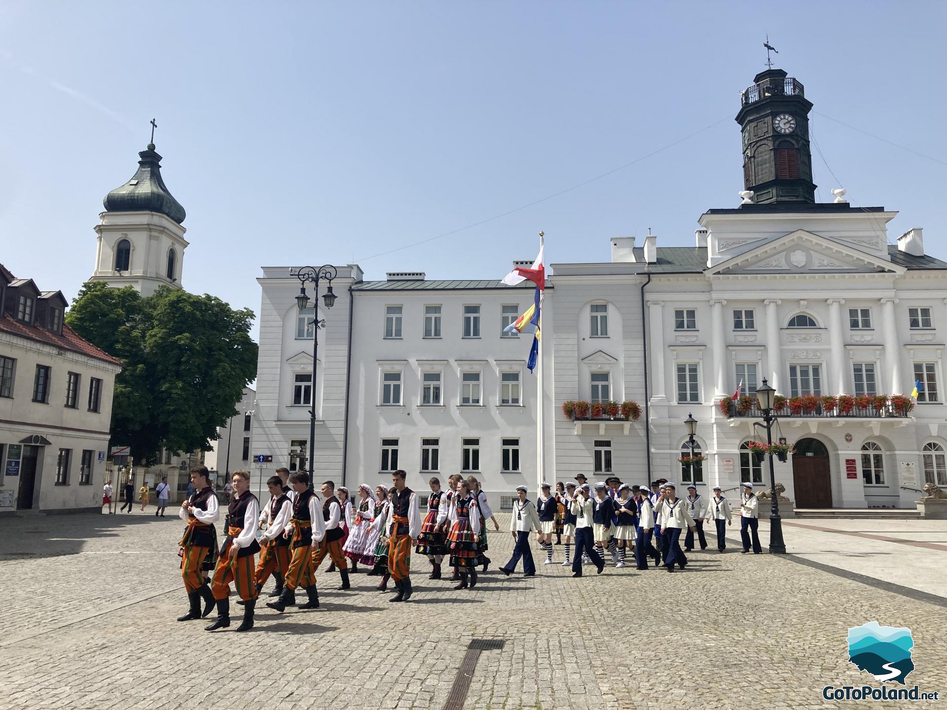 A folk band in front of a white building, girls and boys have nice folk costumes
