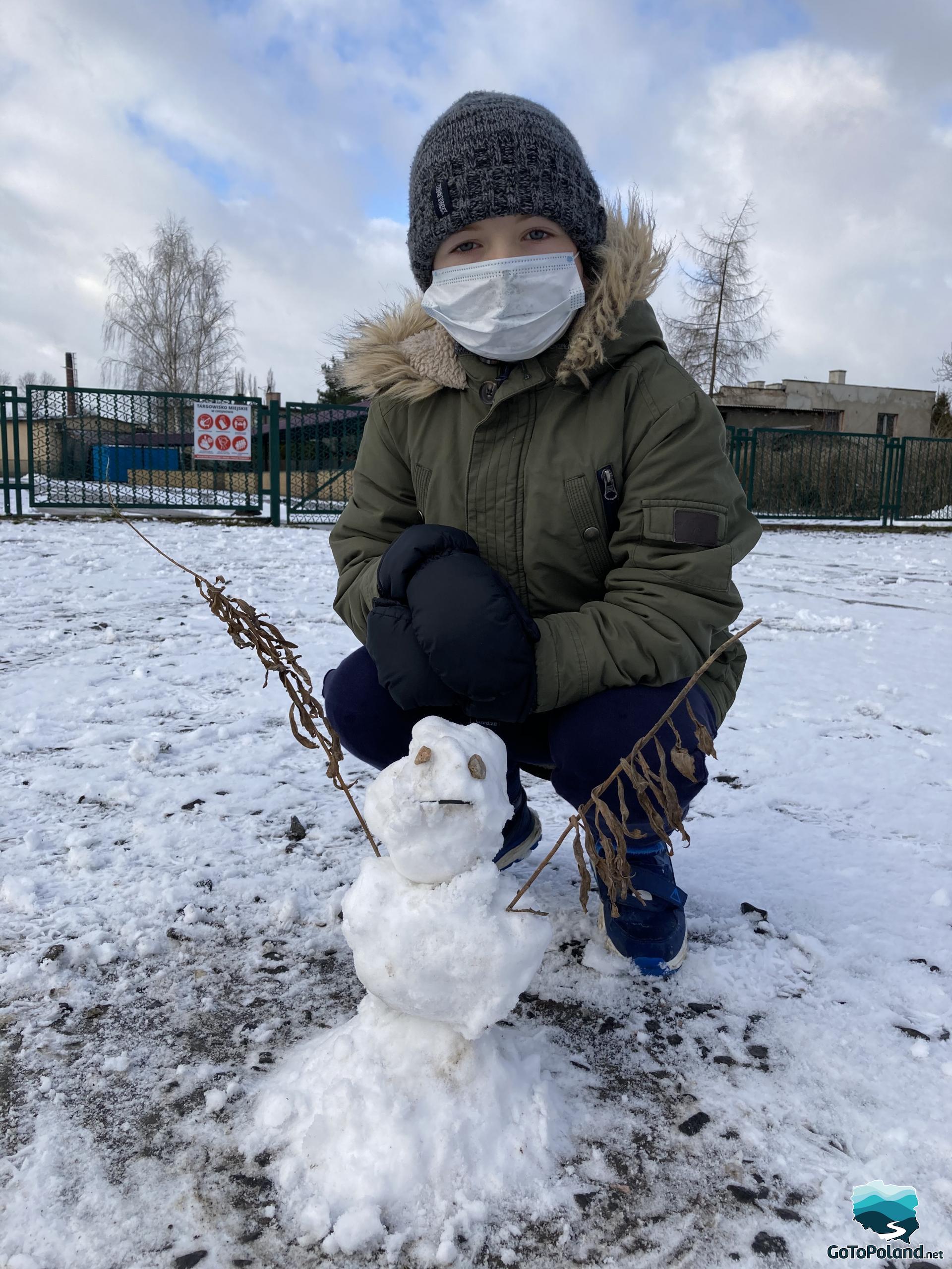 A young boy with a small snowman he made
