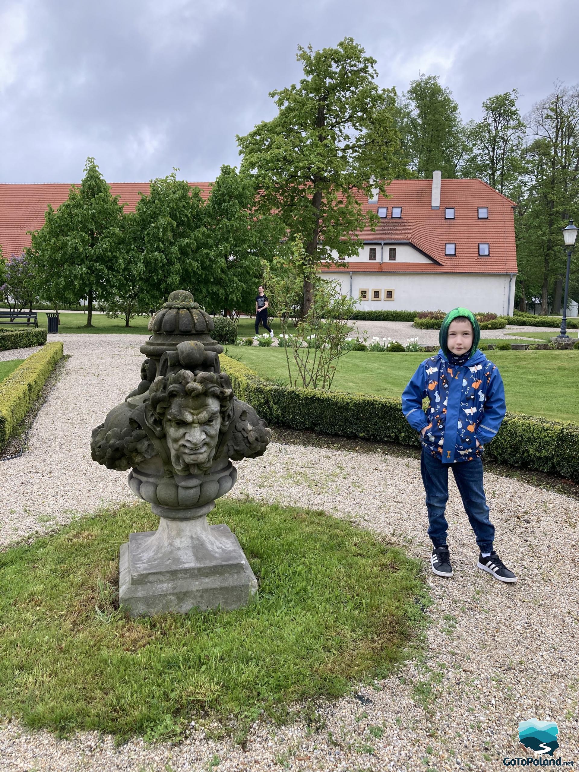 A boy is standing by the stone statue