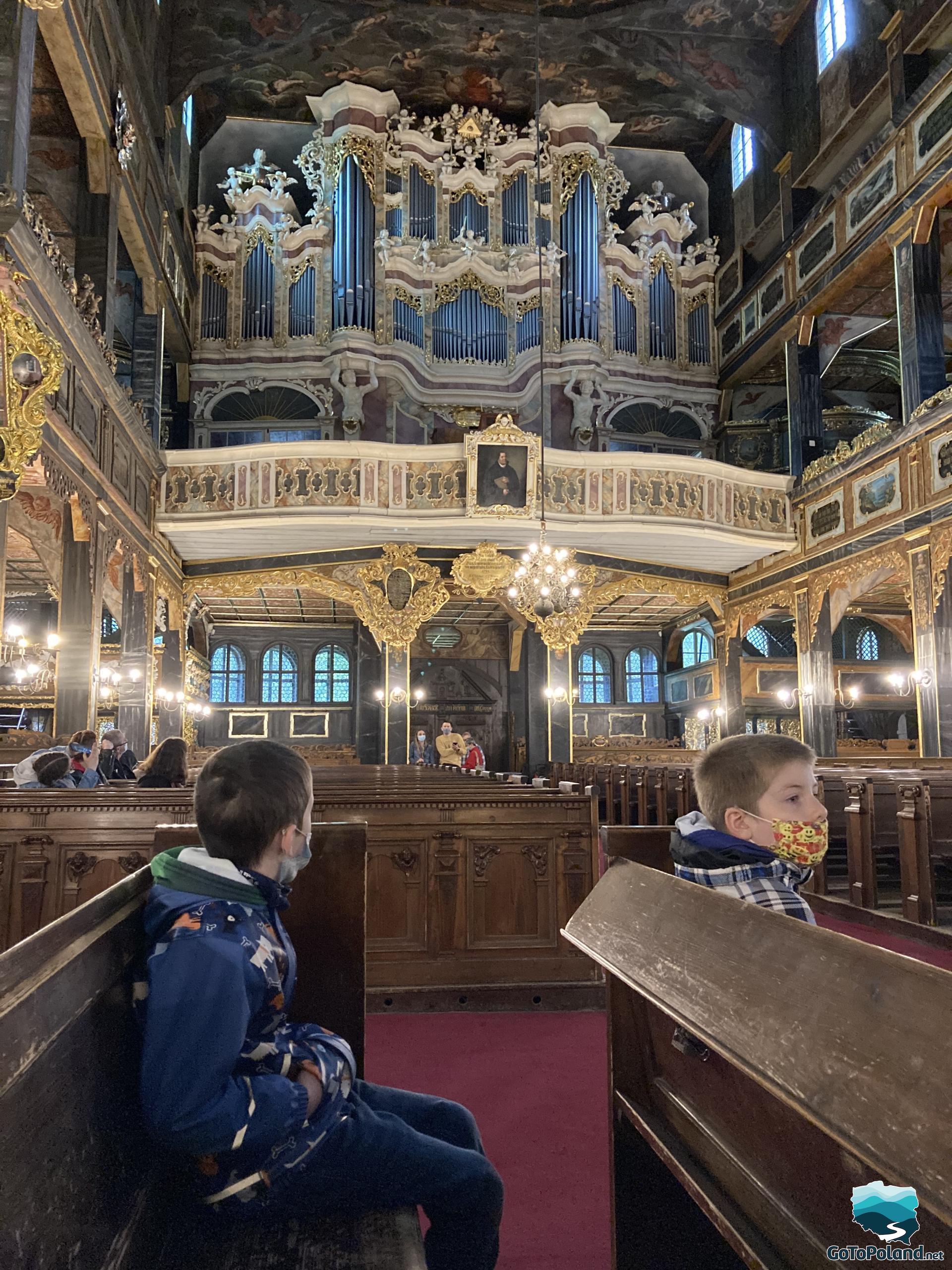 two boy are sitting in the wooden bench, a large organ in the background 