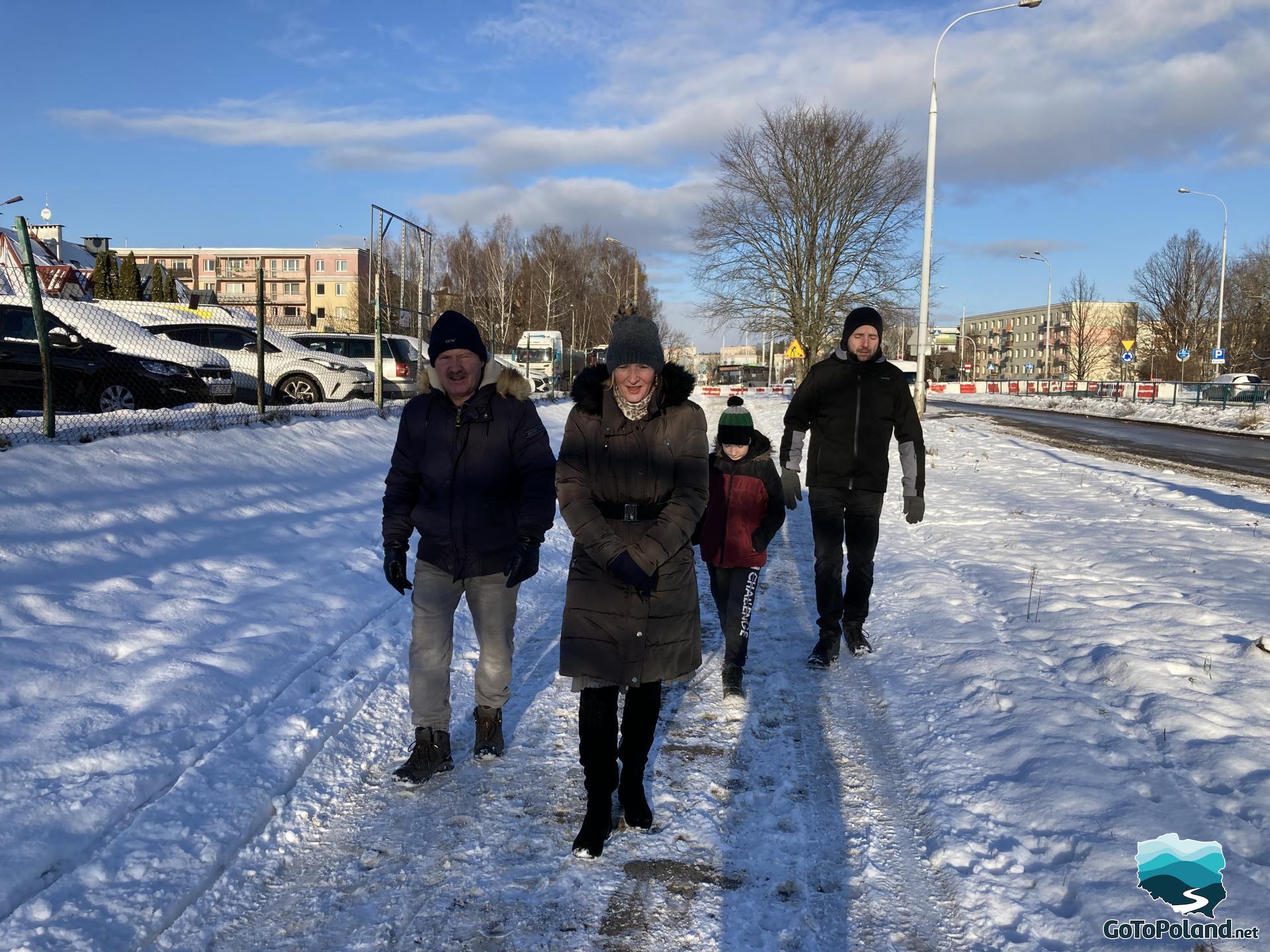 A woman, two men and a child walking along the snowy sidewalk  