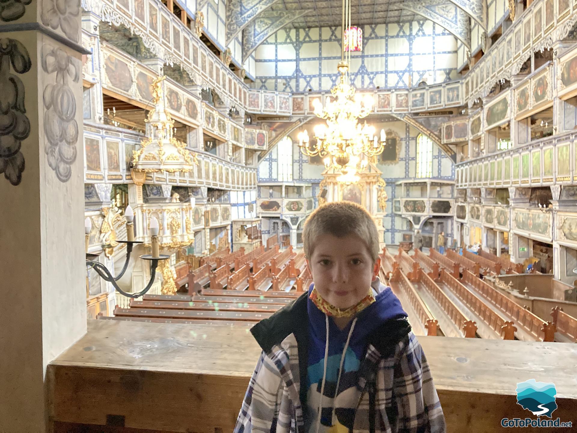 a boy is standing in a church, behind it are rows of benches