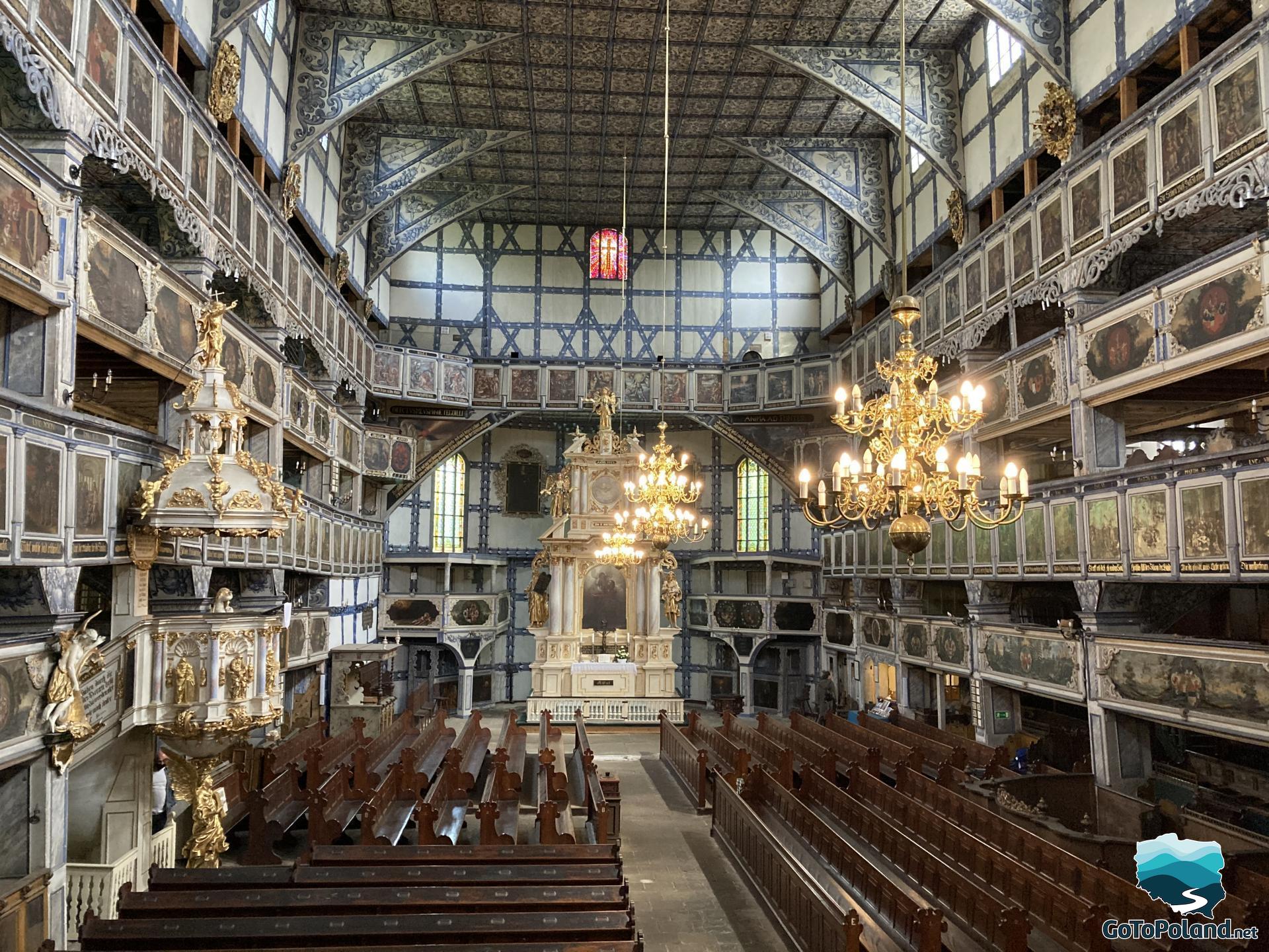 an interior in a church, three chandeliers, rows of benches, a main altar in the background  