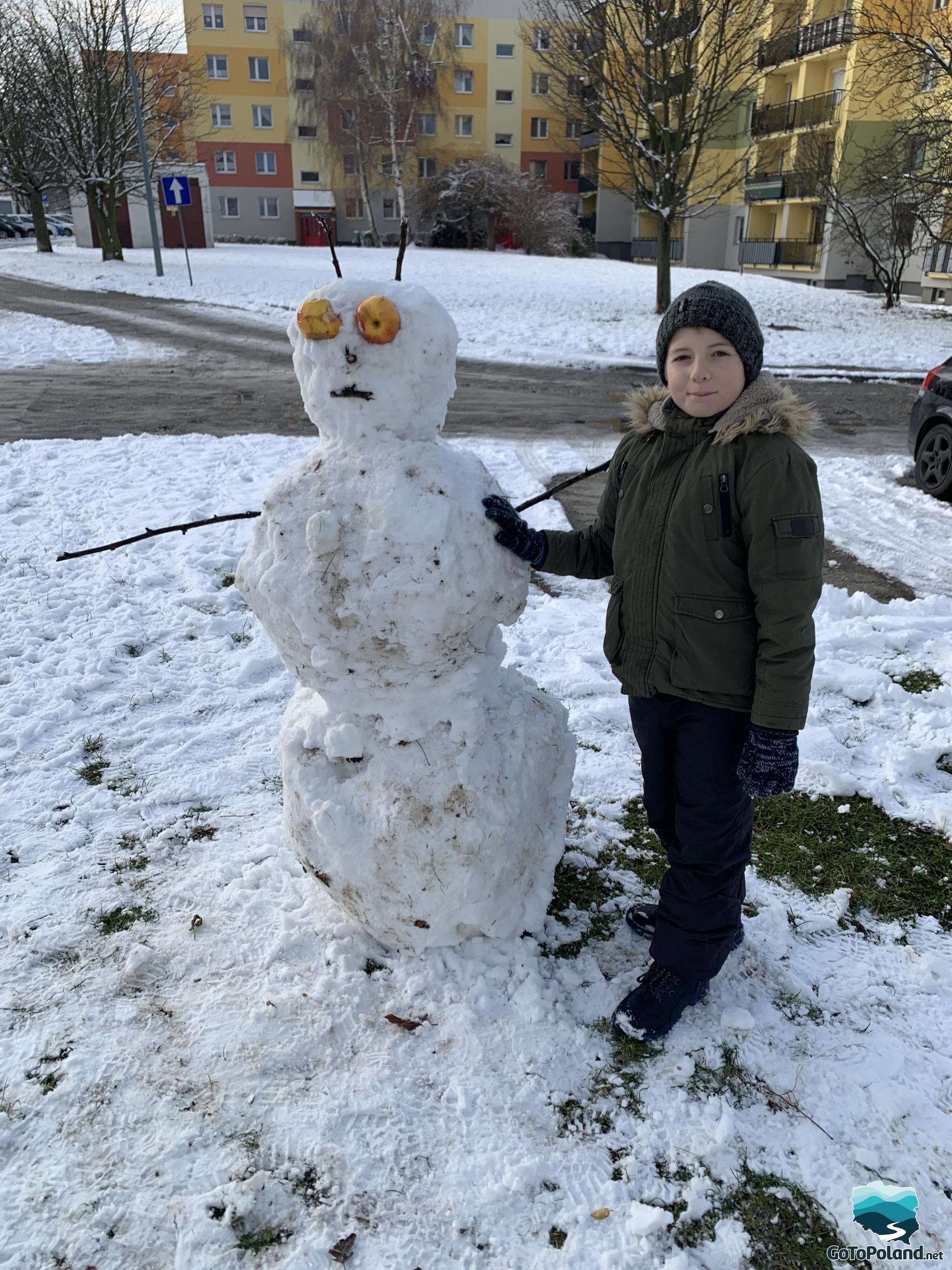 A young boy with a big snowman who has big eyes made of apples 