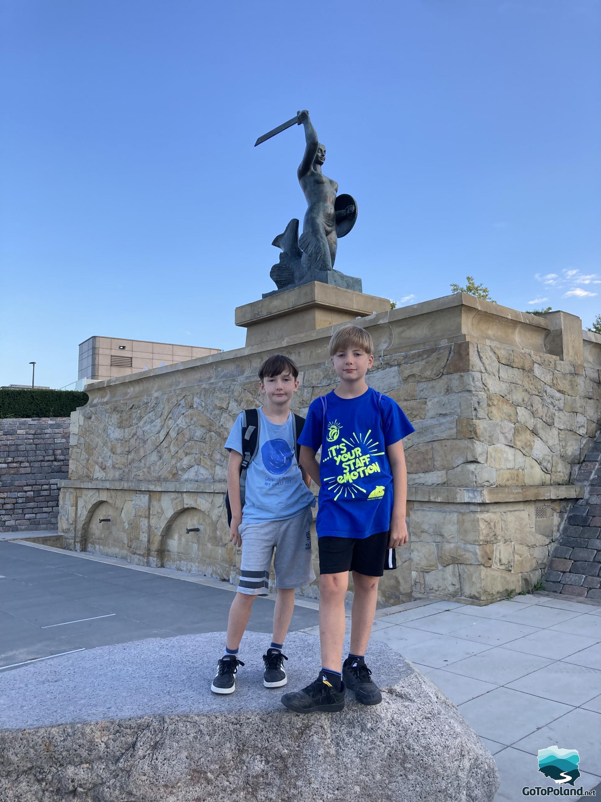 Two boys are standing in front of the mermaid statue
