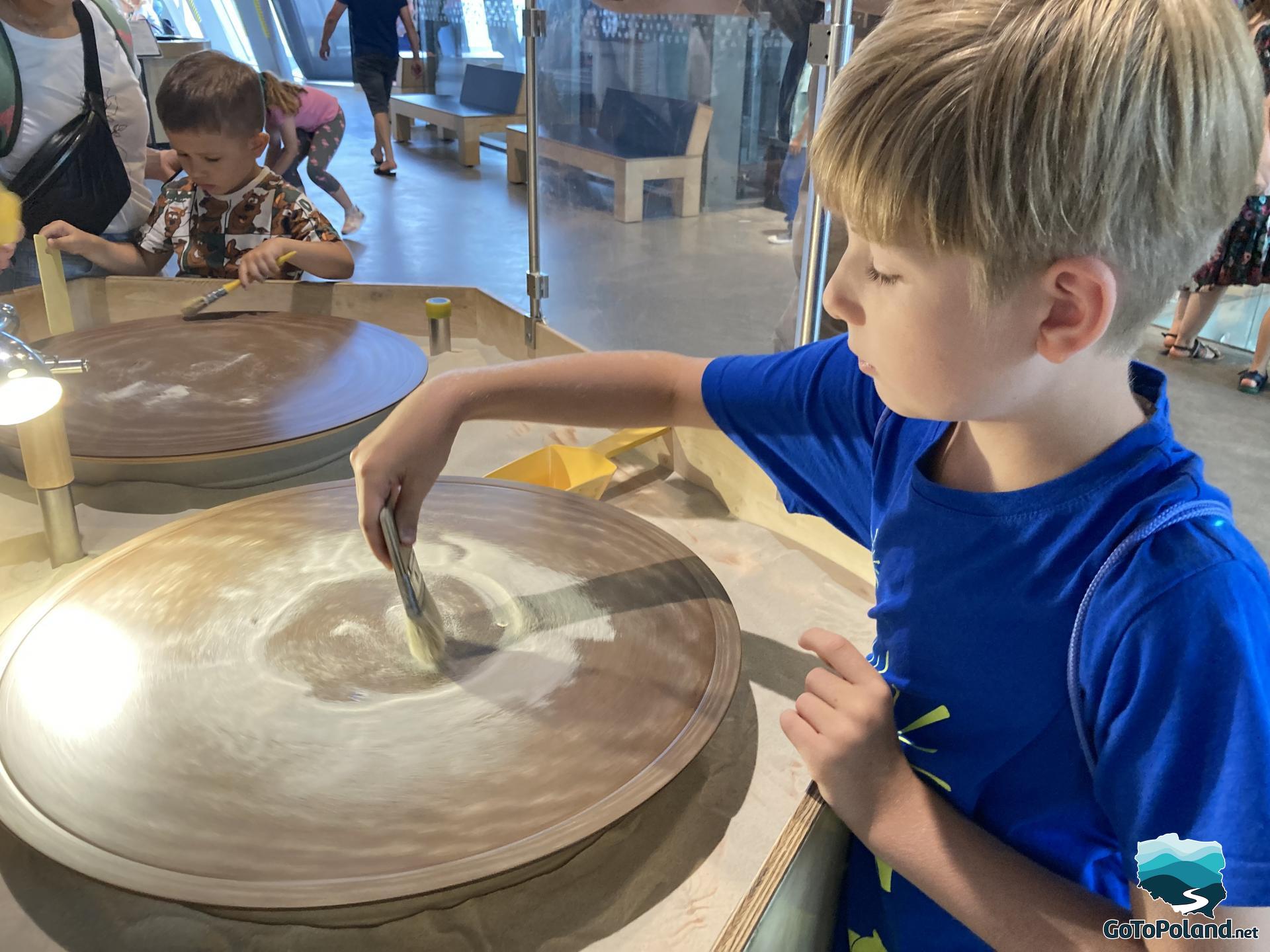 a boy is playing with sand and a wheel in the science centre
