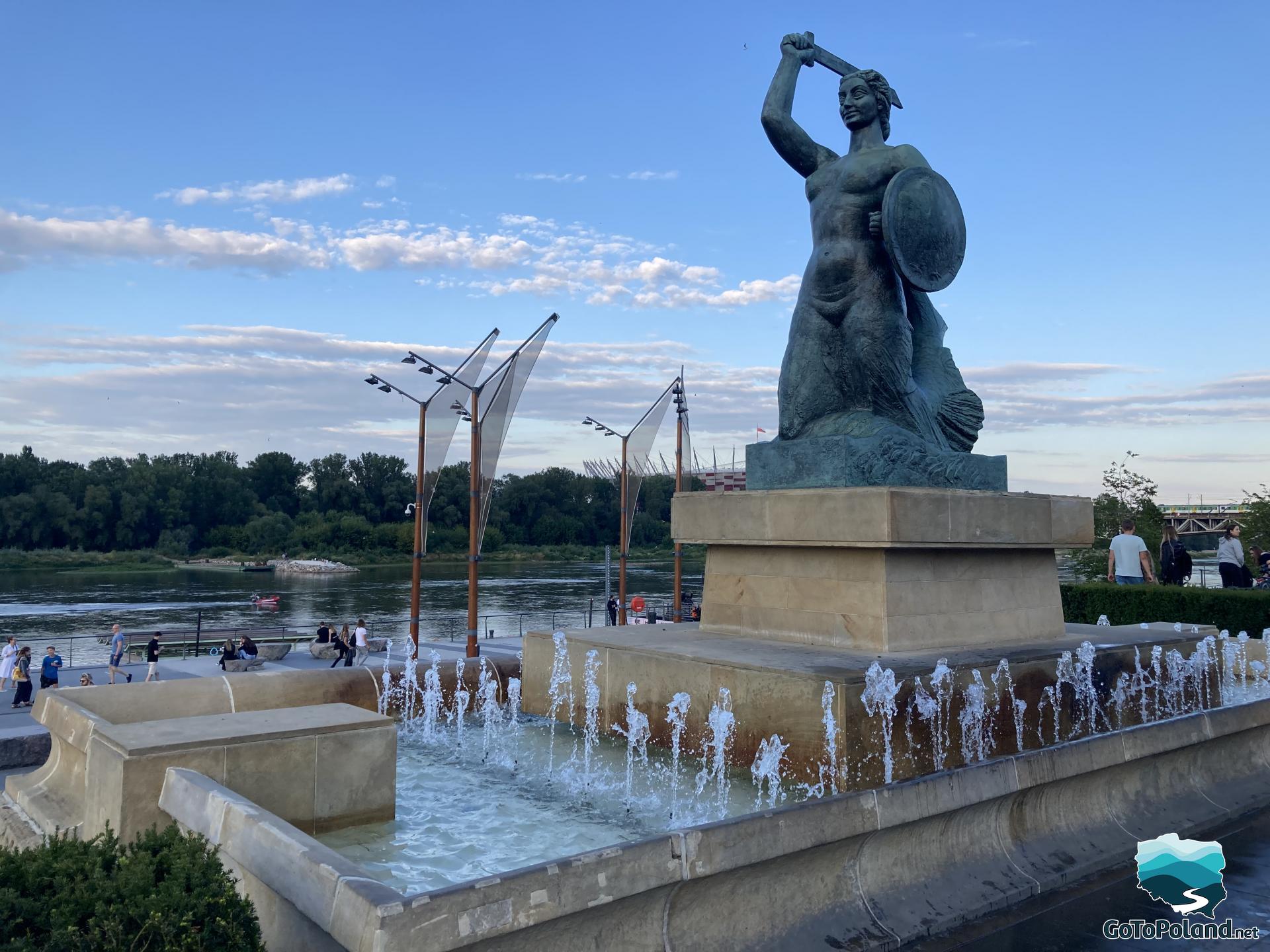 a fountain with a statue of a mermaid, the Vistula River in the background