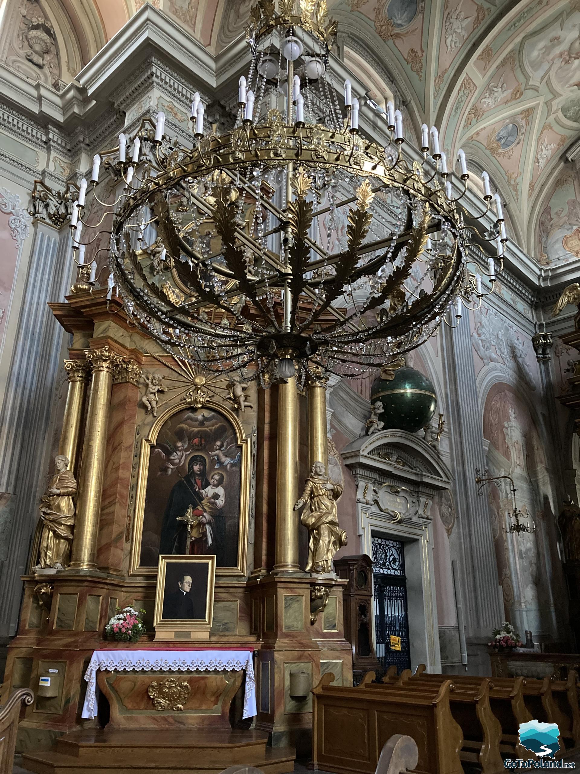 very large chandelier hangs in a church, side altar with the image of Mary