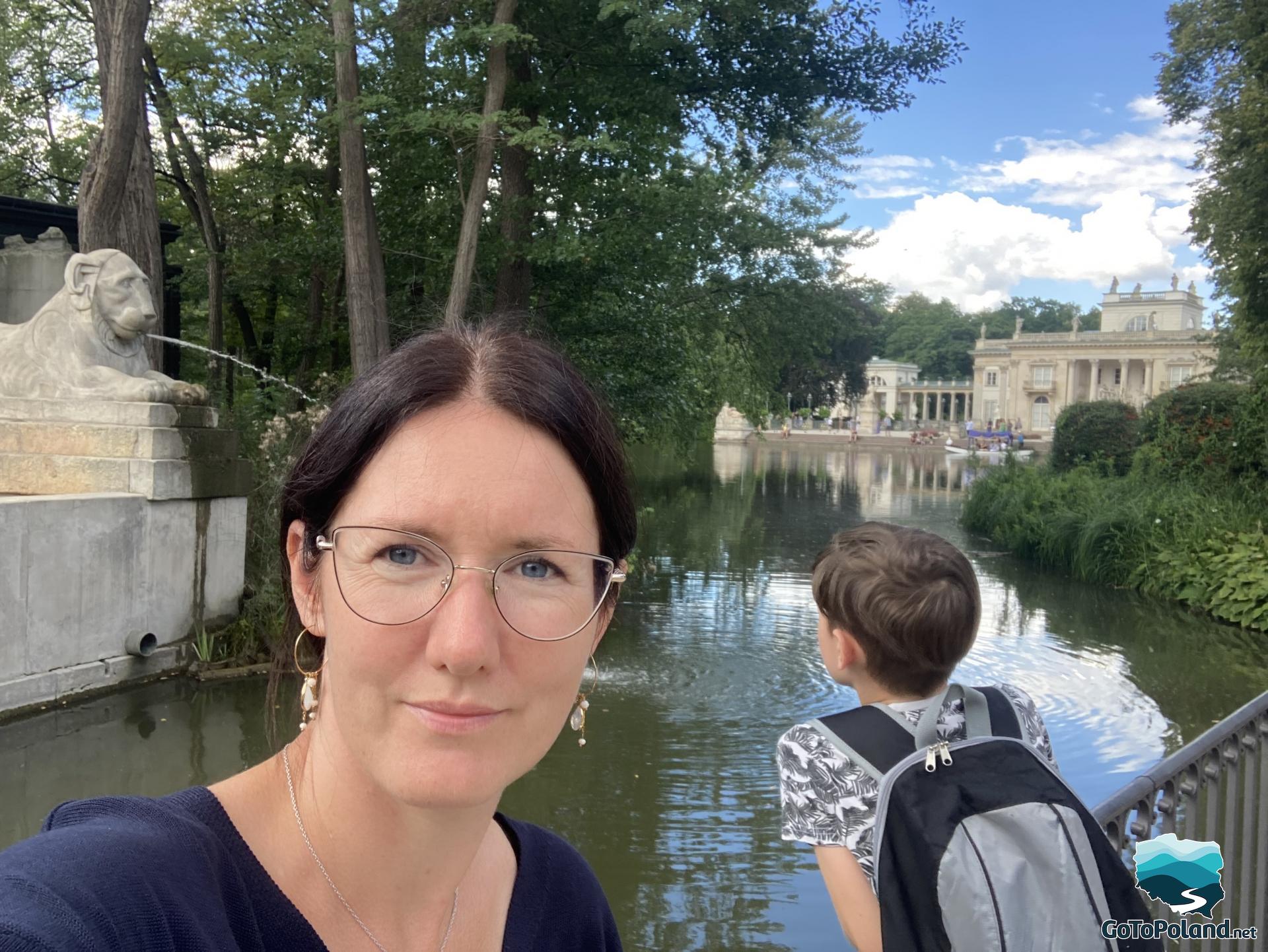 a woman is taking a selfie, next to her is boy, a pond and a palace in the background 