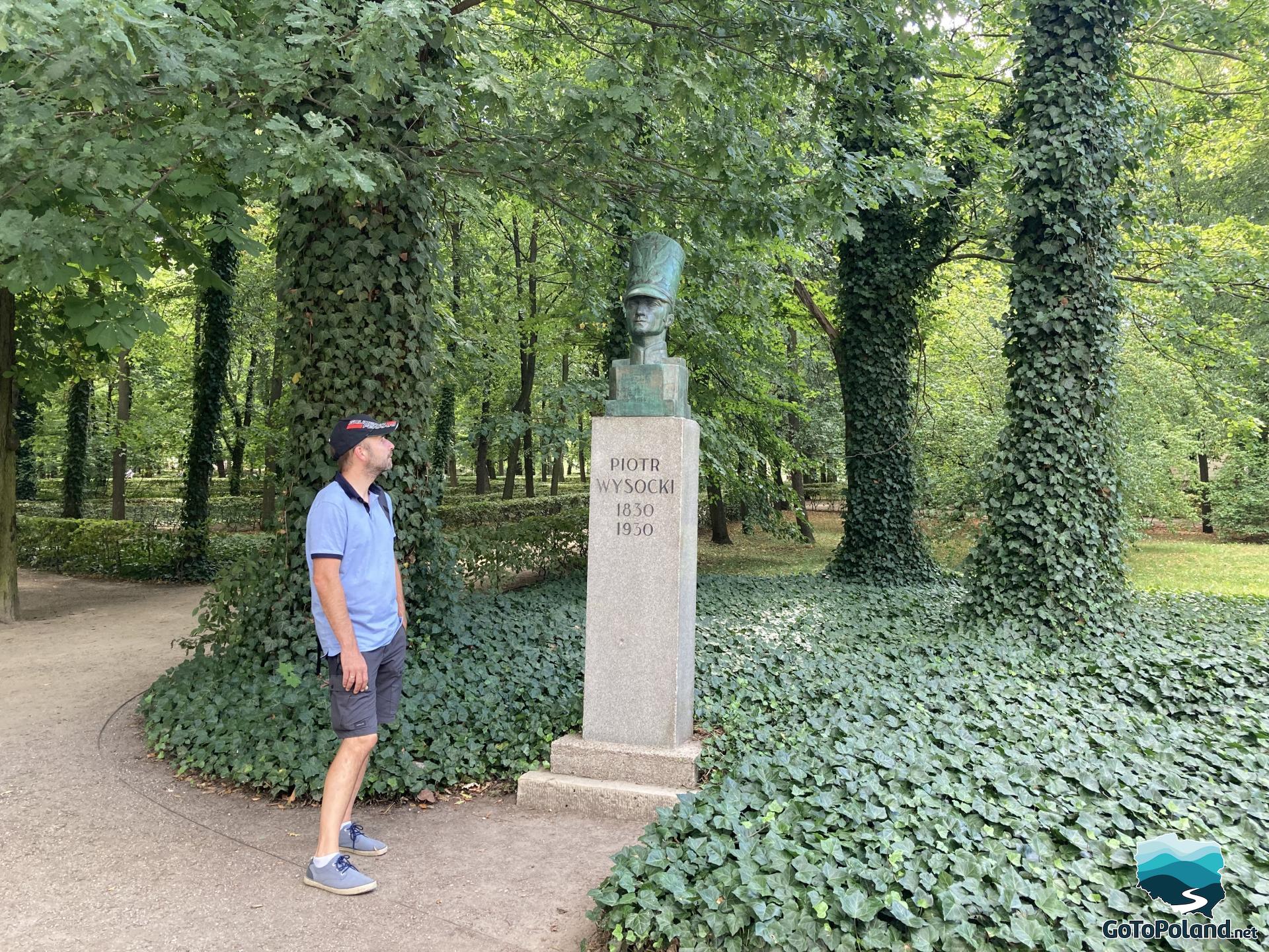 a man is standing in front of the bust of a soldier on a pedestal in a park