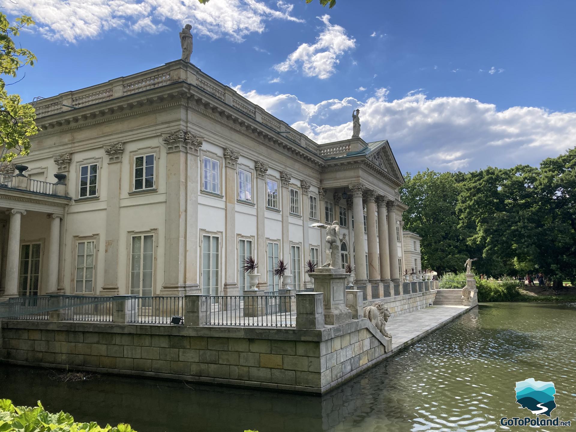 a palace with bright walls, two sculptures of lions and four columns, the palace is located on the water
