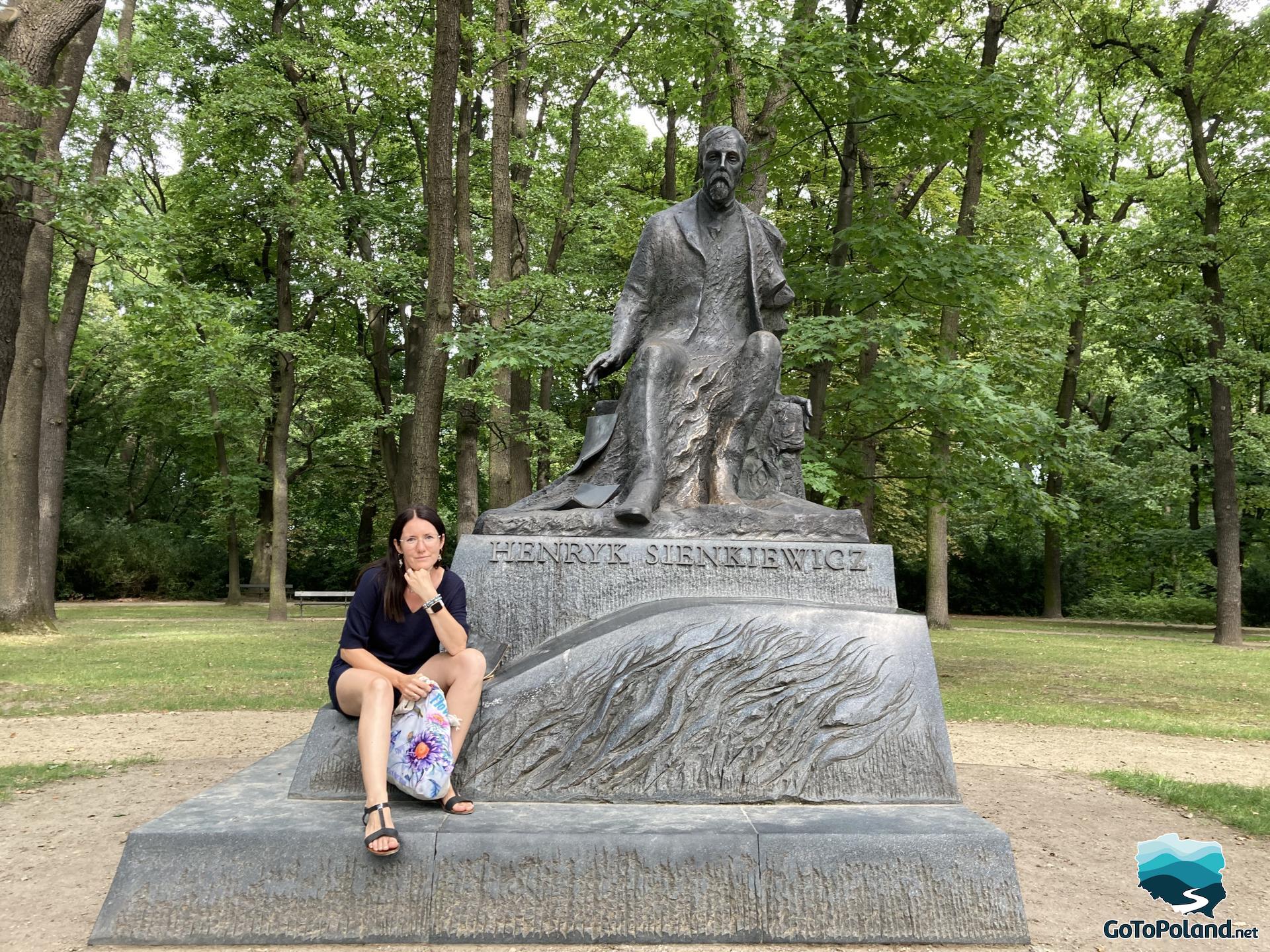 a woman is sitting at the base of a statue of a male writer