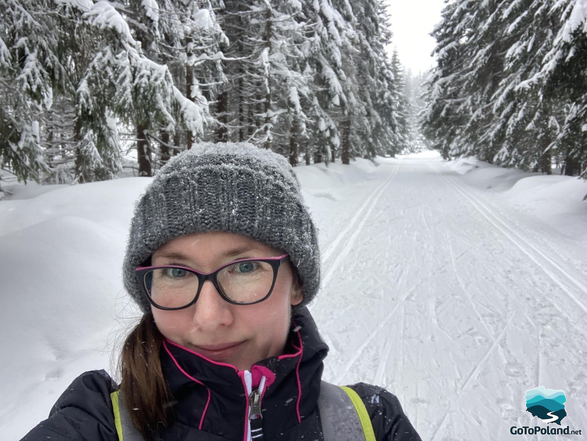 A women in a grey winter hat and a wide, snowy path in the background  