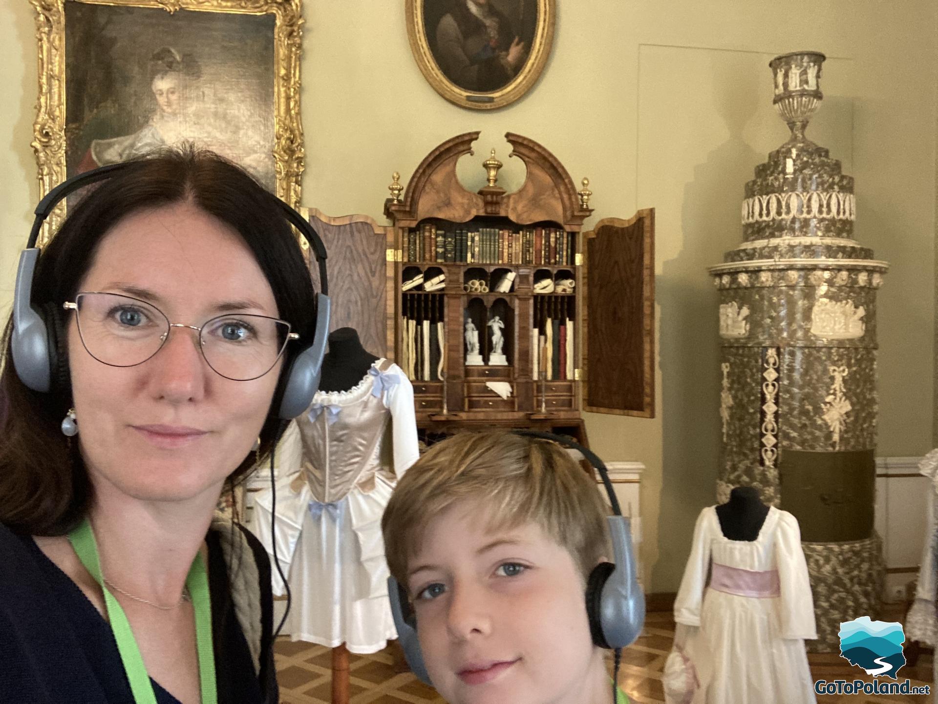 a woman and a boy are taking selfie, behind them there are decorative elements of palace like small bookcase and a painting of woman hangs on the wall
