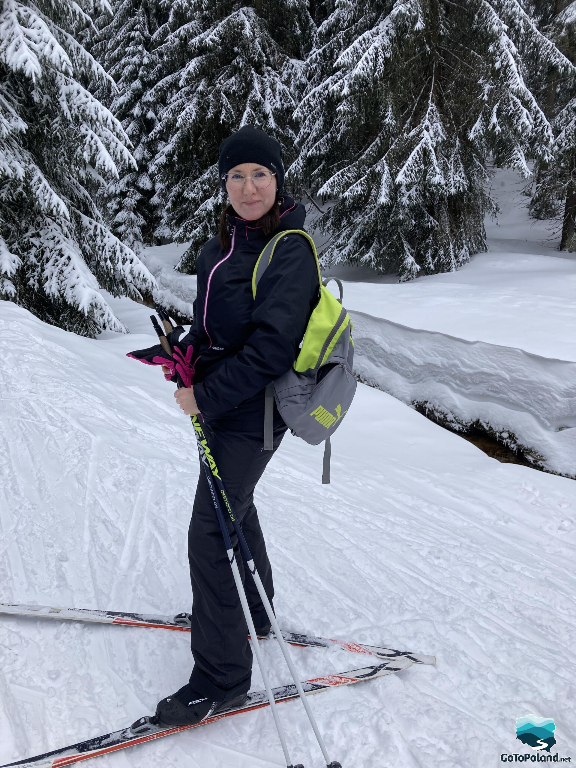 A woman on cross-country skies, spruce trees behind her