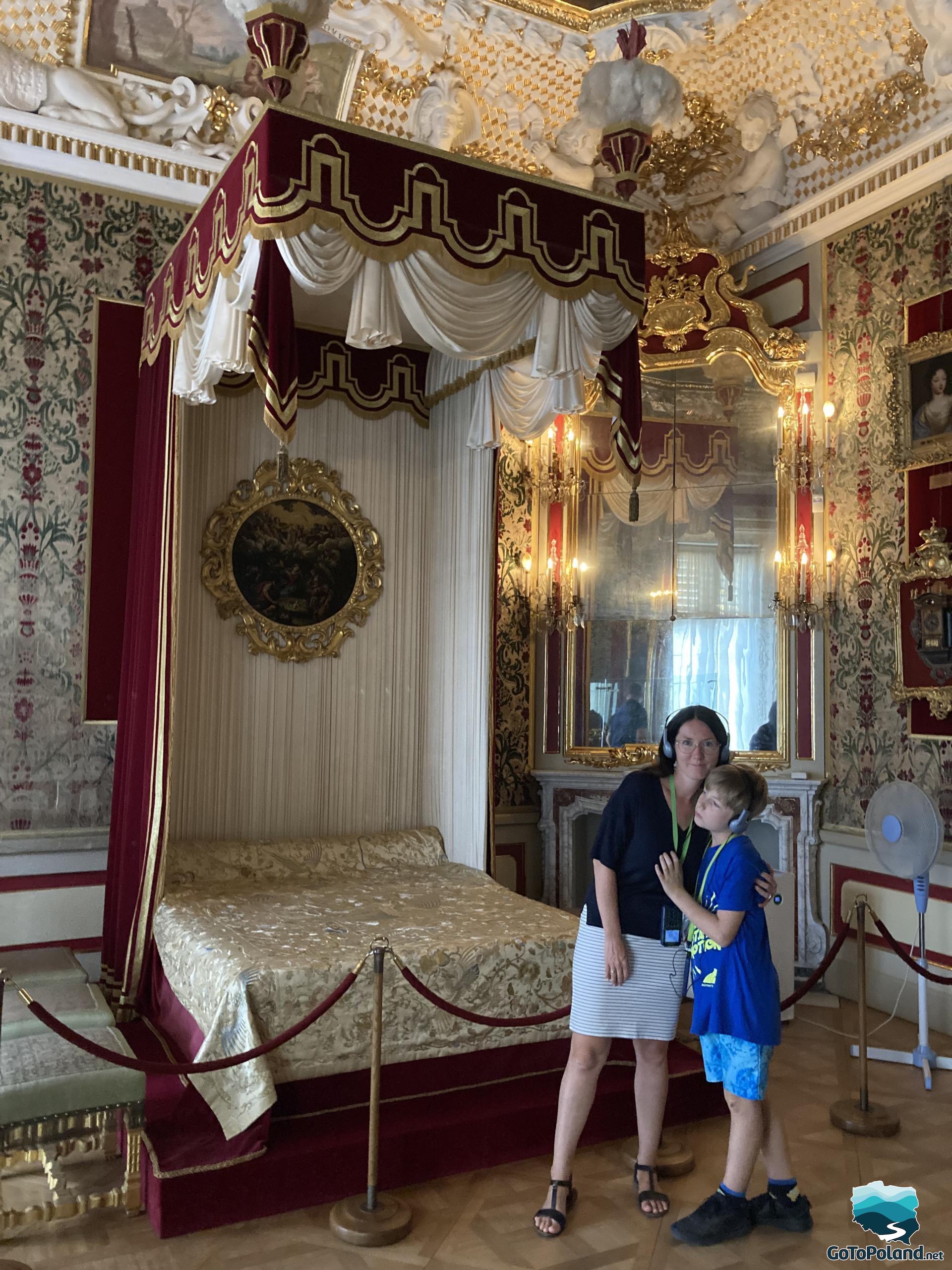 a very decorative bedroom in a palace with a large bed, paintings on the walls, sculptures by the ceiling, a woman with a boy standing next to the bed