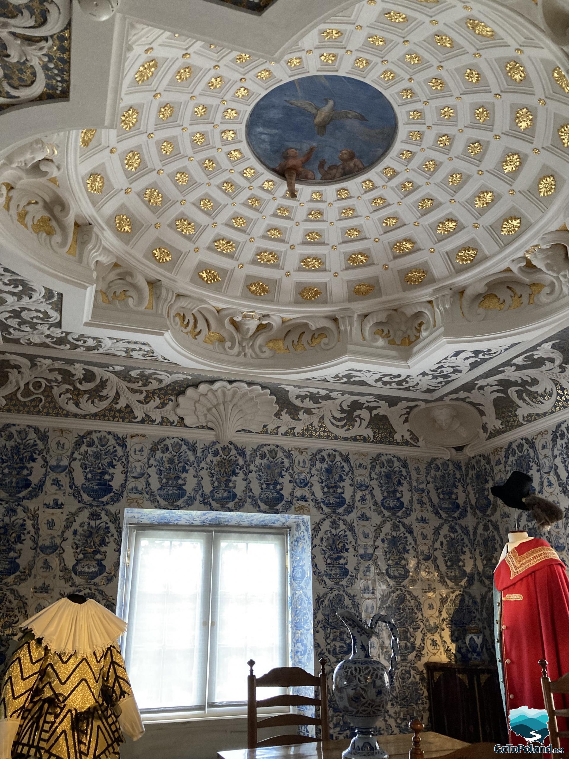 a domed ceiling with a painting of a cupid, the walls of the room decorated with blue decorations, two vintage clothes