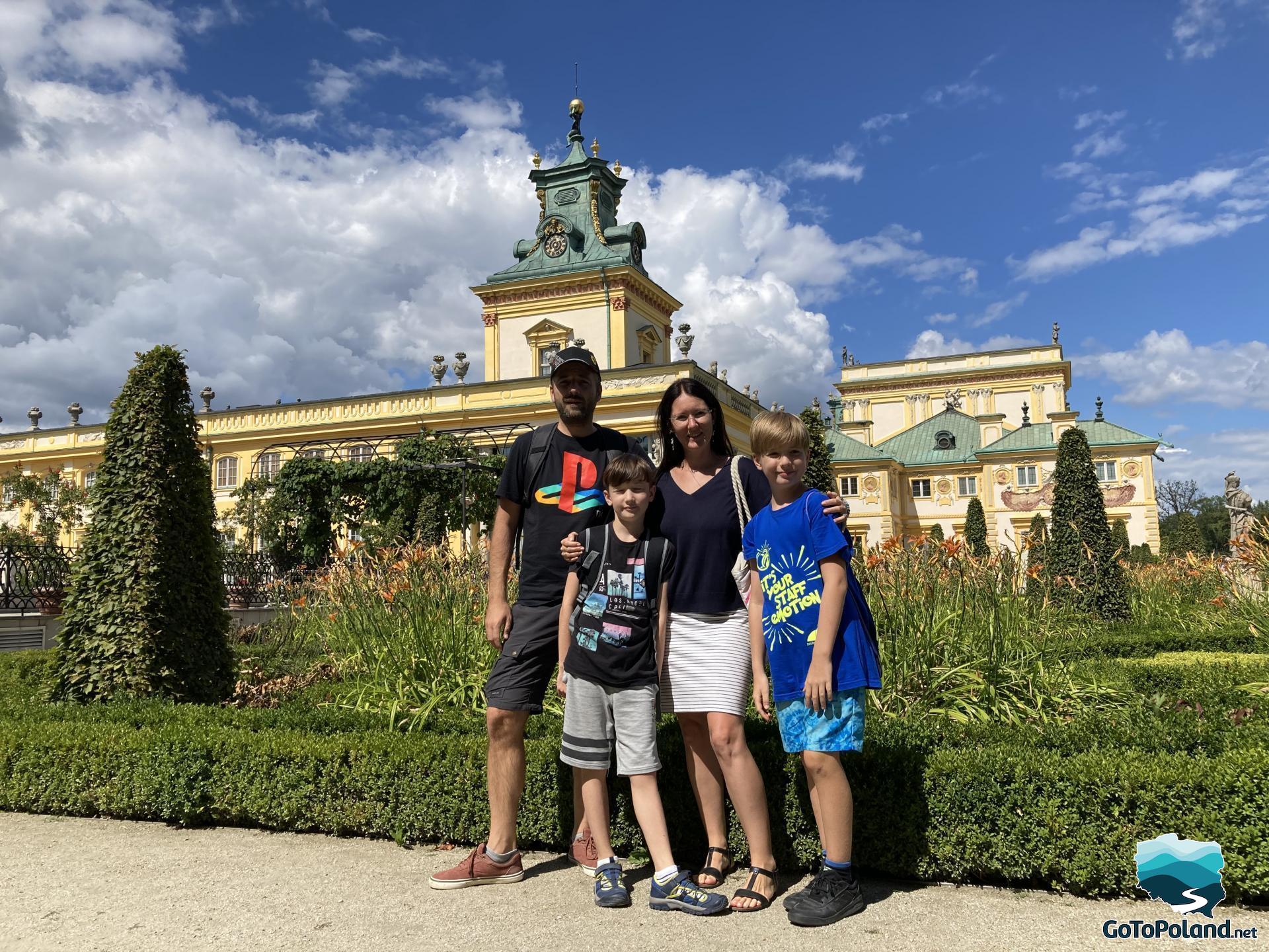 A woman, two boys and a man are standing in the garden which belongs to the palace