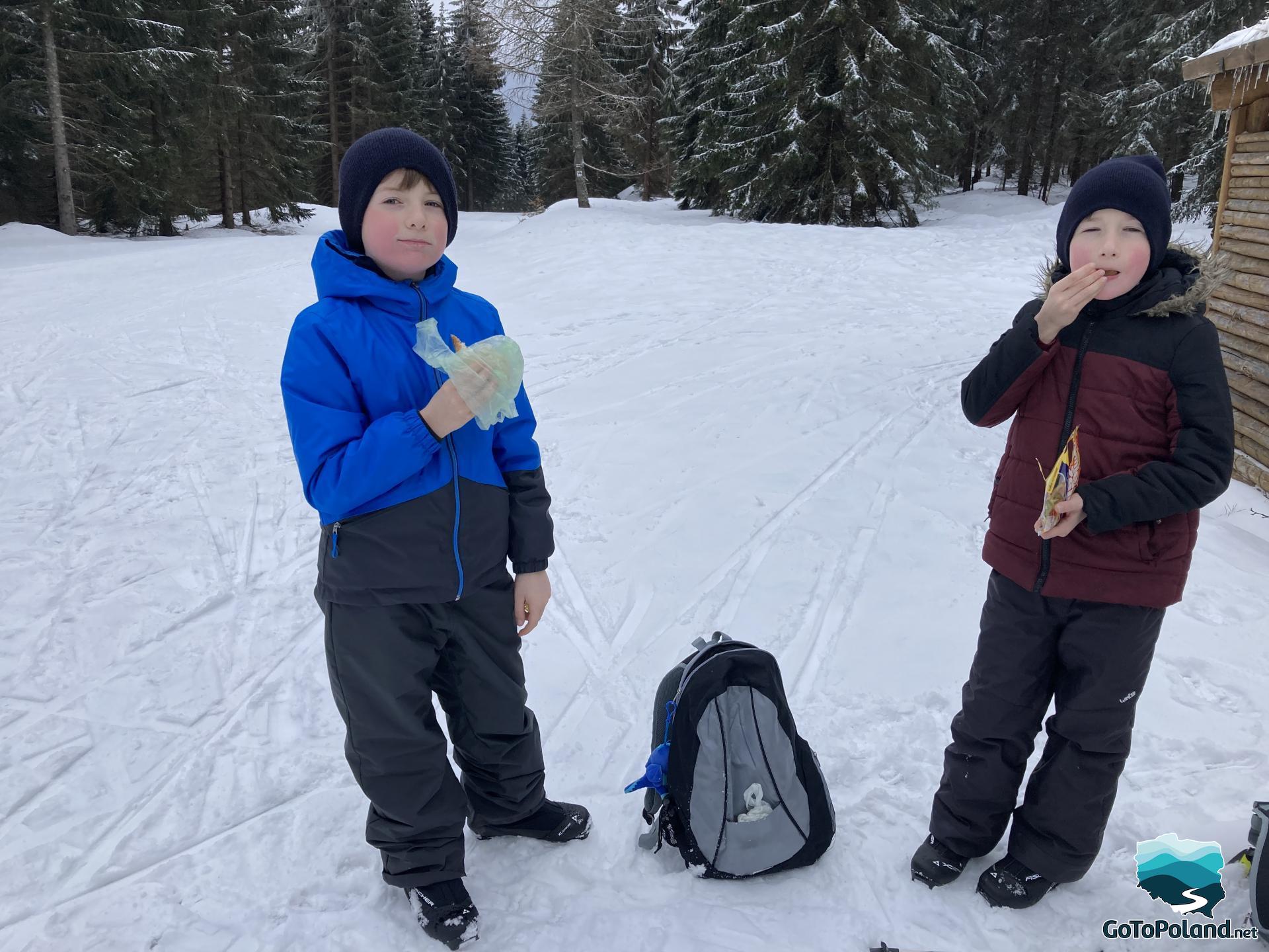 Two young boys are eating sandwiches during short break in Jakuszyce, they are standing on the snow
