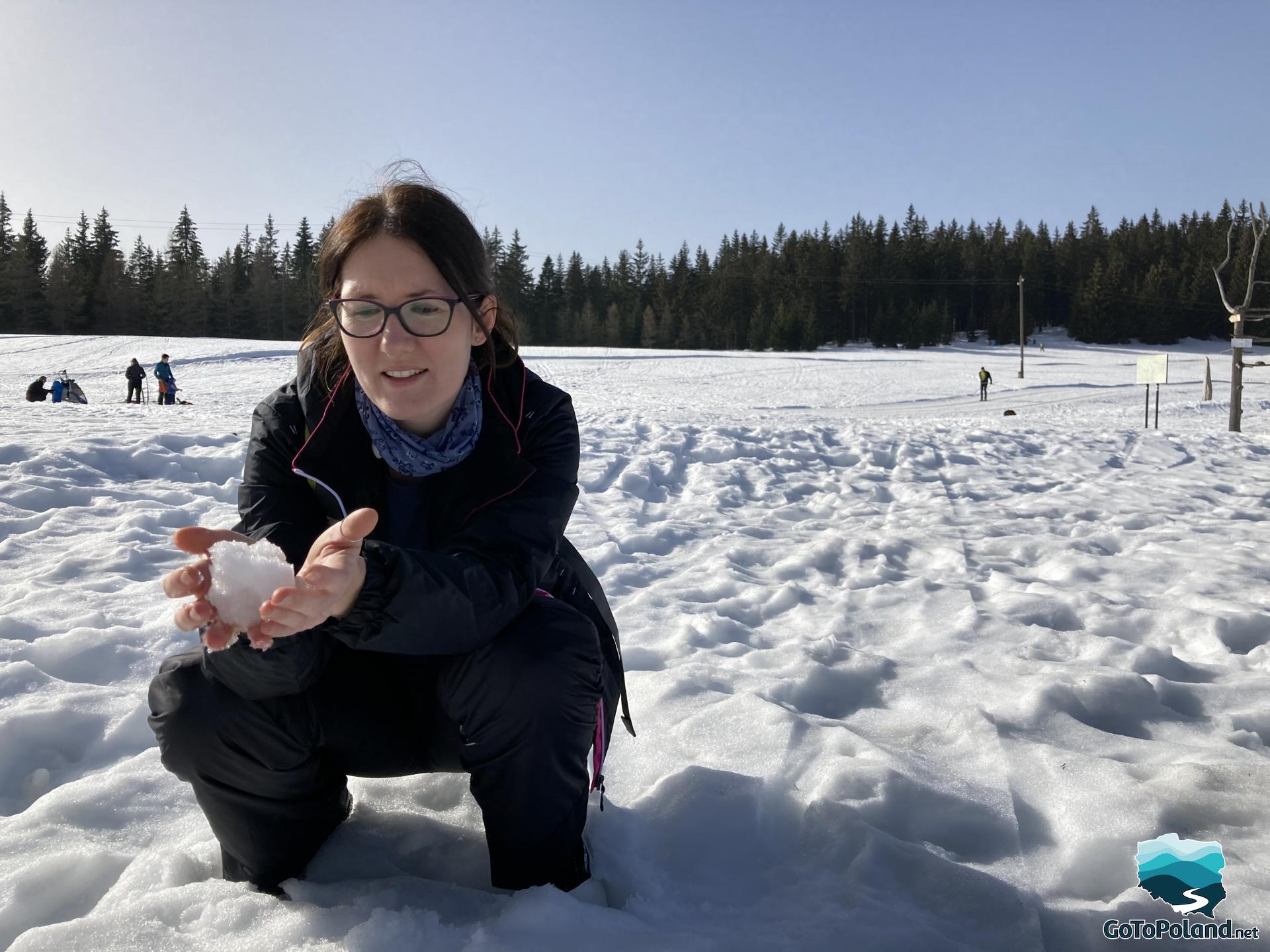 A woman who is crouching in the snow and holding a snowball in her hands
